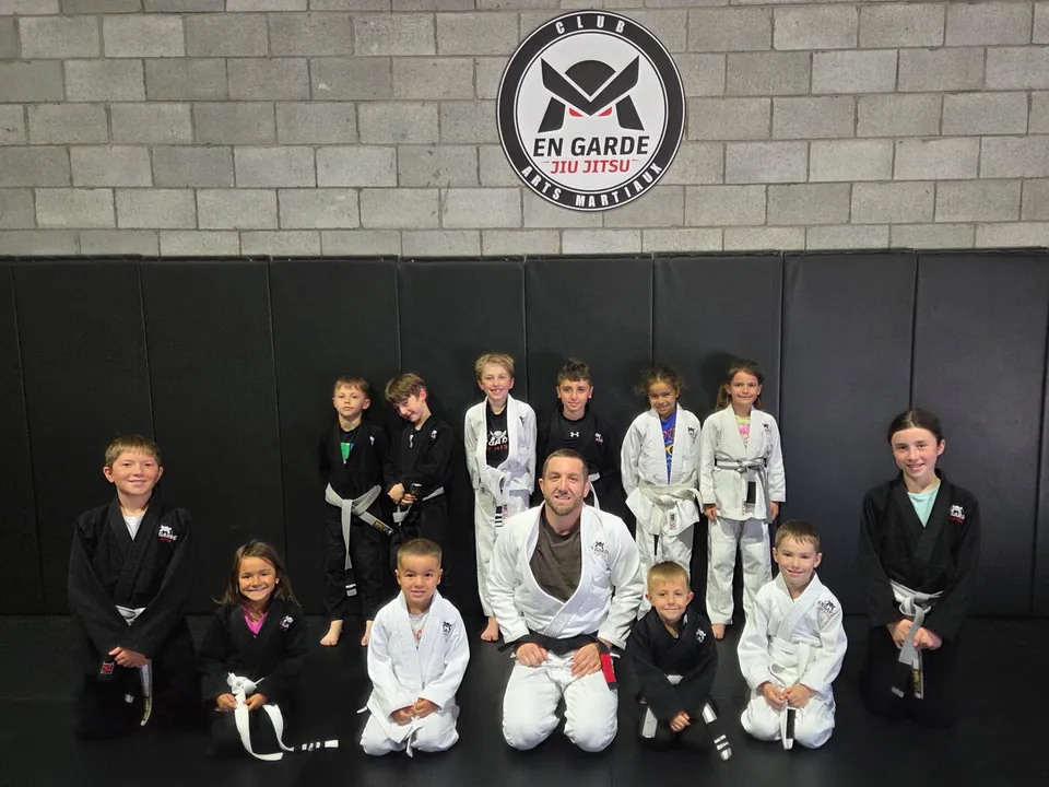 Groupe de jeunes élèves en gi, debout et à genoux autour de leur instructeur, devant le logo du club En Garde Jiu-Jitsu